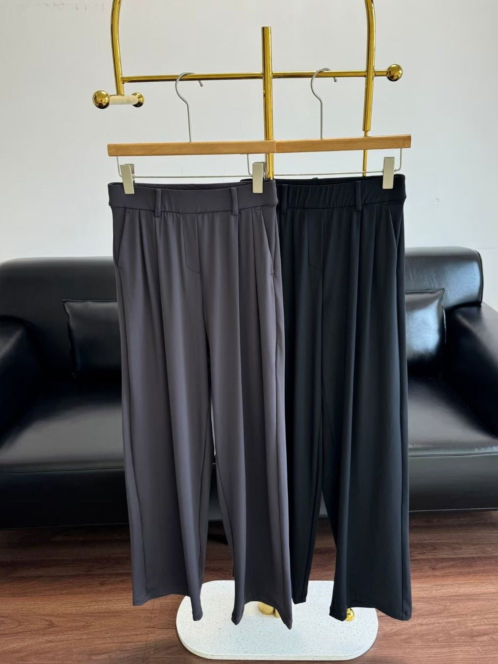 Black pants hanging on a gold rack with a black sofa in the background